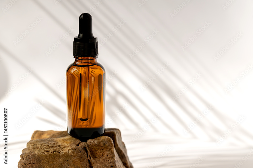Dark glass cosmetic bottles with a dropper on a beige background with stones and tropical leaves. Natural cosmetics concept, natural essential oil and skin care products - obrazy, fototapety, plakaty 