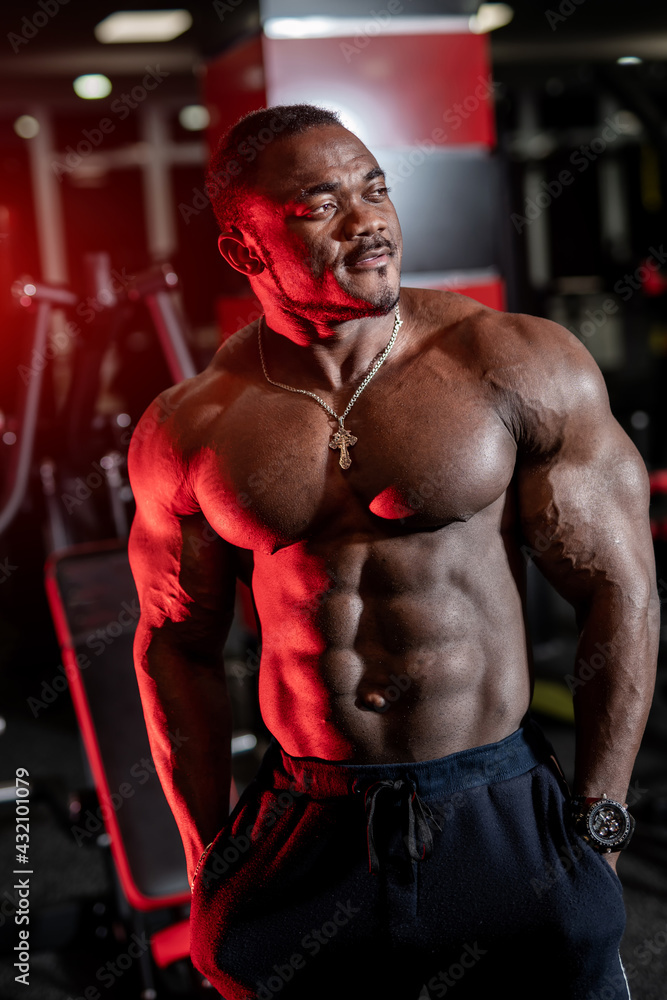 Fototapeta premium Strong halfnaked african american bodybuilder standing in contemporary gym and looking away.