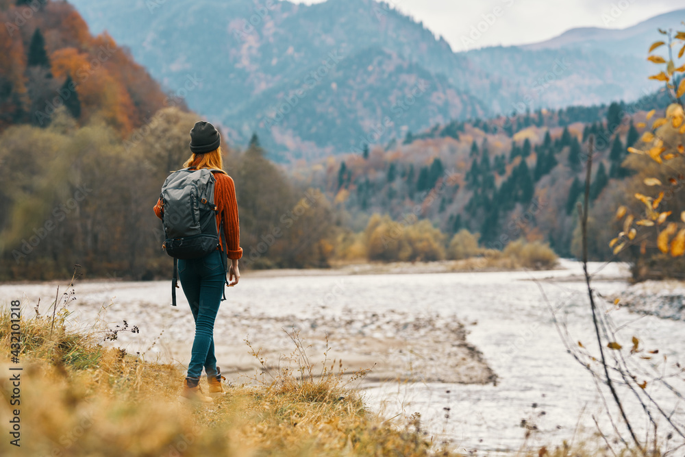 woman on the river bank in the mountains in the autumn forest in nature back view