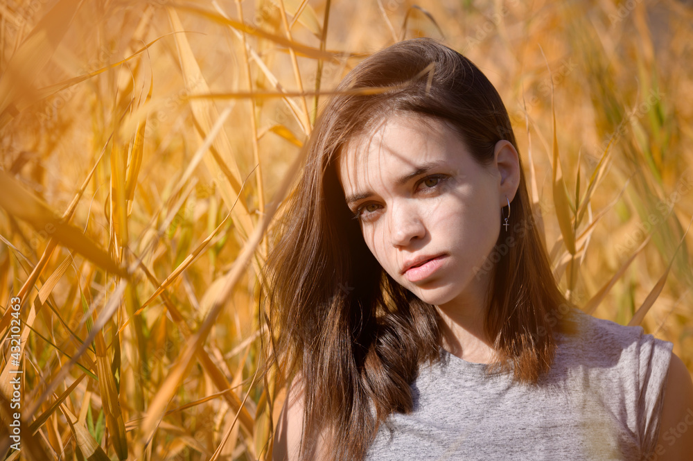 Portrait of an attractive young woman in a T-shirt with an enigmatic look stands among the yellow reeds and looks at the camera Portrait of an attractive young woman in a T-shirt with an enigmatic look stands among the yellow reeds and looks at the camera