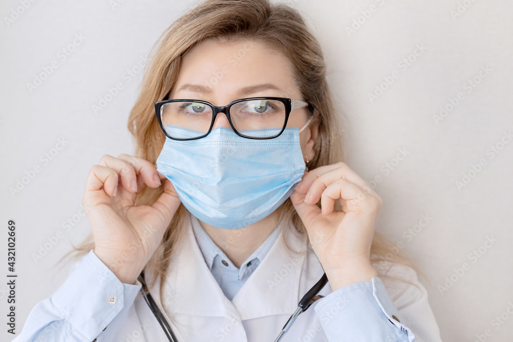 Portrait of female doctor putting on a blue protective mask, cover up her face. Caucasian woman in medical uniform is looking at the camera, reminds to take care of yourself while coronavirus pandemic