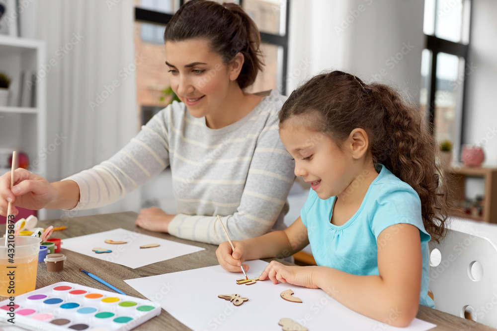 family, hobby and leisure concept - happy smiling mother spending time with her little daughter drawing or painting wooden chipboard items with colors at home family, hobby and leisure concept - happy smiling mother spending time with her little daughter drawing or painting wooden chipboard items with colors at home