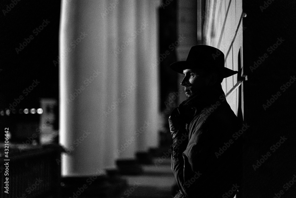 dark silhouette of a man in a raincoat with a hat and a scar on his face at night