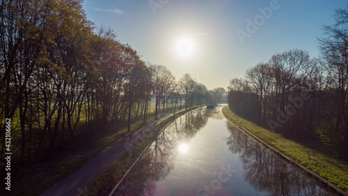 Aerial view of an Idillic river stream canal with grass banks and wild flowers and trees in a scenic landscape on a misty sunny spring morning sunrise day, taken with a drone. High quality photo