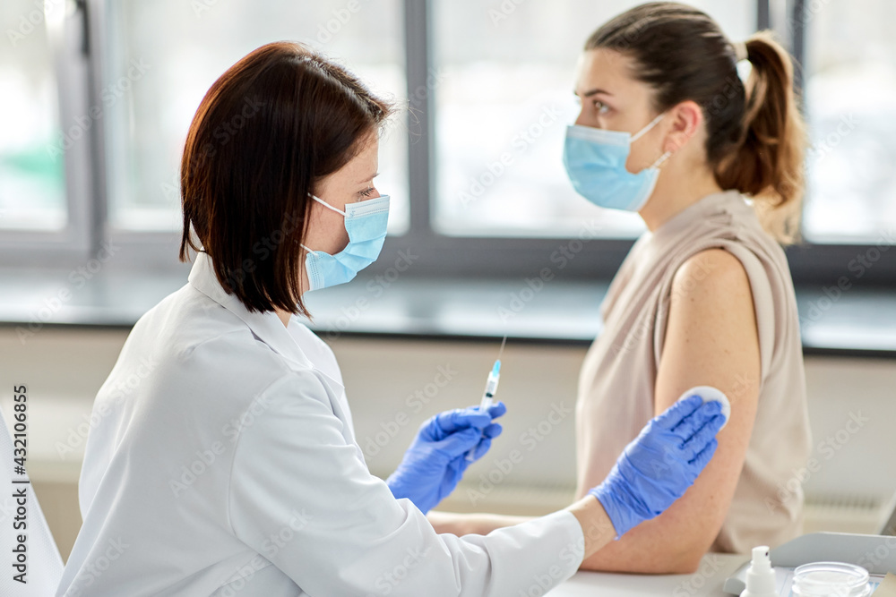 health, medicine and pandemic concept - female doctor or nurse wearing protective medical mask with syringe vaccinating patient at hospital health, medicine and pandemic concept - female doctor or nurse wearing protective medical mask with syringe vaccinating patient at hospital