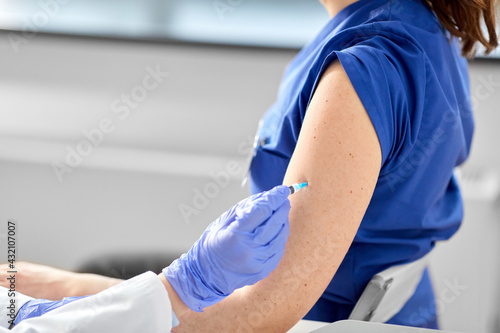 health  medicine and pandemic concept - close up of female doctor or nurse wearing protective medical gloves with syringe vaccinating medical worker hospital