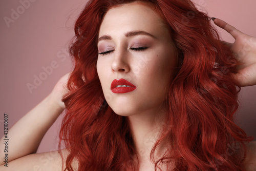 Close-up of beautiful young woman with red hair posing over pink background. 