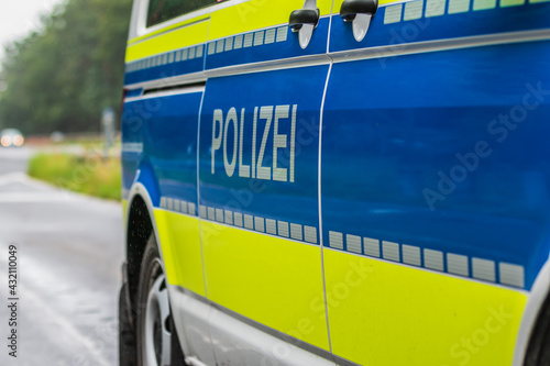 Side view of a German police car. Police lettering on the body from the passenger side. Blue background and yellow color with reflective stripes. Highway in the background