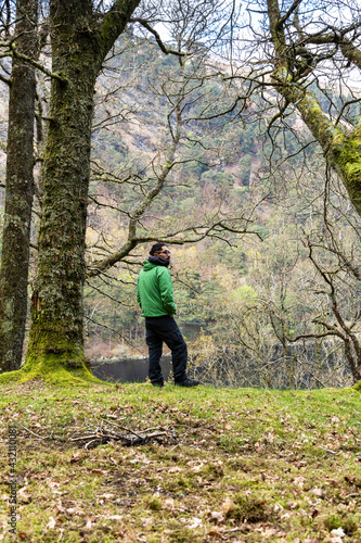 A Man in green jacket standing in forest admiring the landscape © Simon