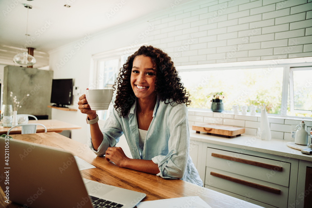 Mixed race female student working from home drinking hot coffee smiling typing on laptop Mixed race female student working from home drinking hot coffee smiling typing on laptop