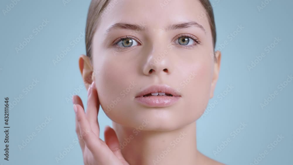 Headshot of pretty woman turning head and looking to camera while touching face with one hand . Female attractive model with nude make up posing . Concept of cosmetology, skincare. Headshot of pretty woman turning head and looking to camera while touching face with one hand . Female attractive model with nude make up posing . Concept of cosmetology, skincare.