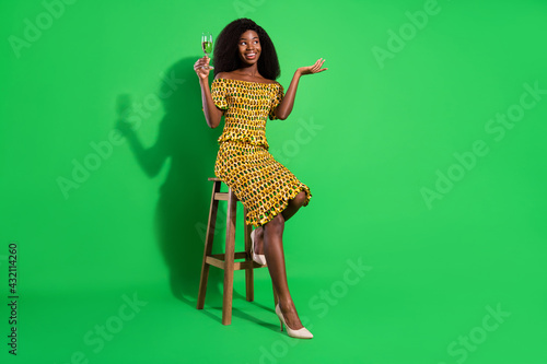 Full size photo of attractive black woman happy positive smile sit bar drink champagne isolated over green color background