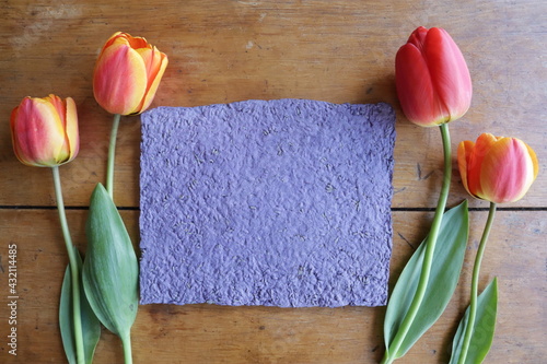 Fototapeta Naklejka Na Ścianę i Meble -  Four tulips over a wood table makes a perfect present and layout for any motive, space for a message and a lovely text on a handmade purple paper, made with love