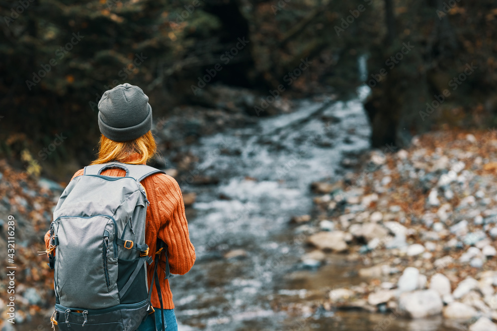 woman near the river in the mountains with a backpack on her shoulders are resting in the autumn forest woman near the river in the mountains with a backpack on her shoulders are resting in the autumn forest
