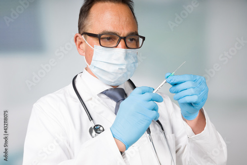 doctor with medical face mask and medical gloves presenting a syringe pulled up with a coronavirus vaccine