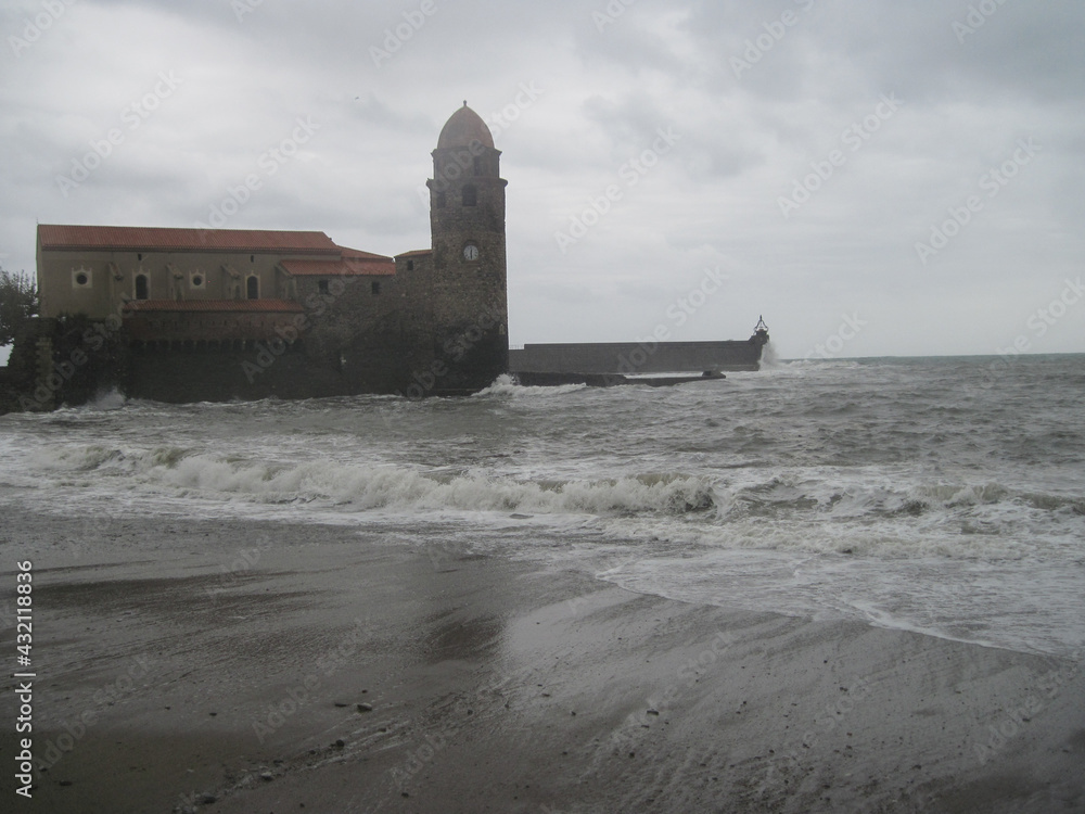 Scenic view of historical castle on the town shore in Collioure, France. Dynamic gray coastline background with storm of the Mediterranean Sea on a cloudy rainy day. Scenic view of historical castle on the town shore in Collioure, France. Dynamic gray coastline background with storm of the Mediterranean Sea on a cloudy rainy day.