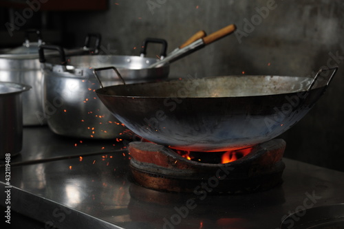 Chef cooking with a wok in fire on charcoal in a kitchen (Asian food, Thai Chinese culinary)