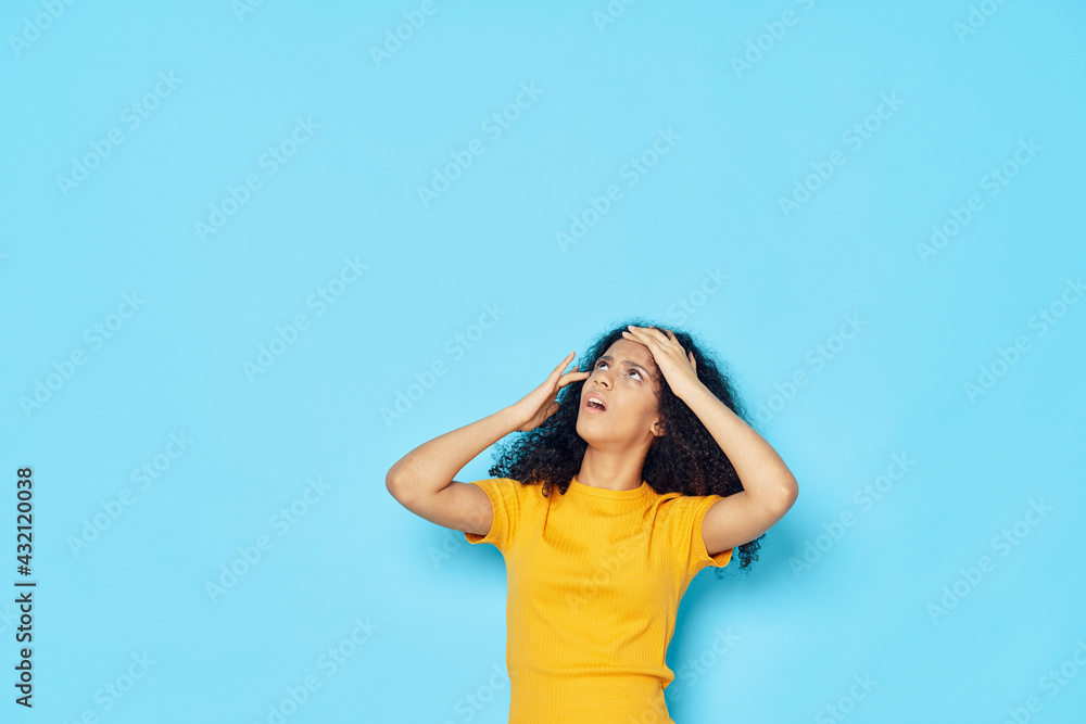 Obraz premium woman with curly hair in a yellow t-shirt holding her head emotions studio
