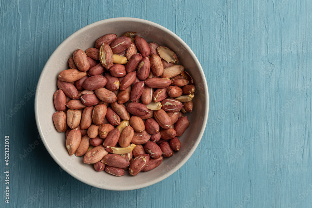 One bowl full of peeled peanuts on a blue background One bowl full of peeled peanuts on a blue background