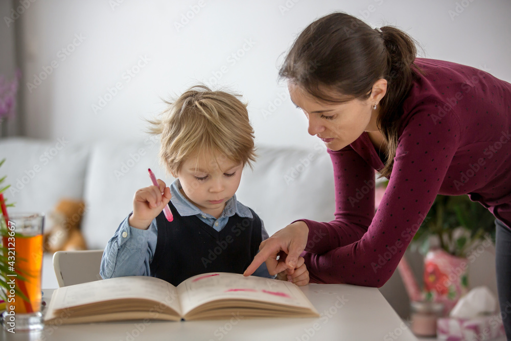 Cute preschool child, blond boy, filling some homework in a work book and coloring, mother helping him Cute preschool child, blond boy, filling some homework in a work book and coloring, mother helping him