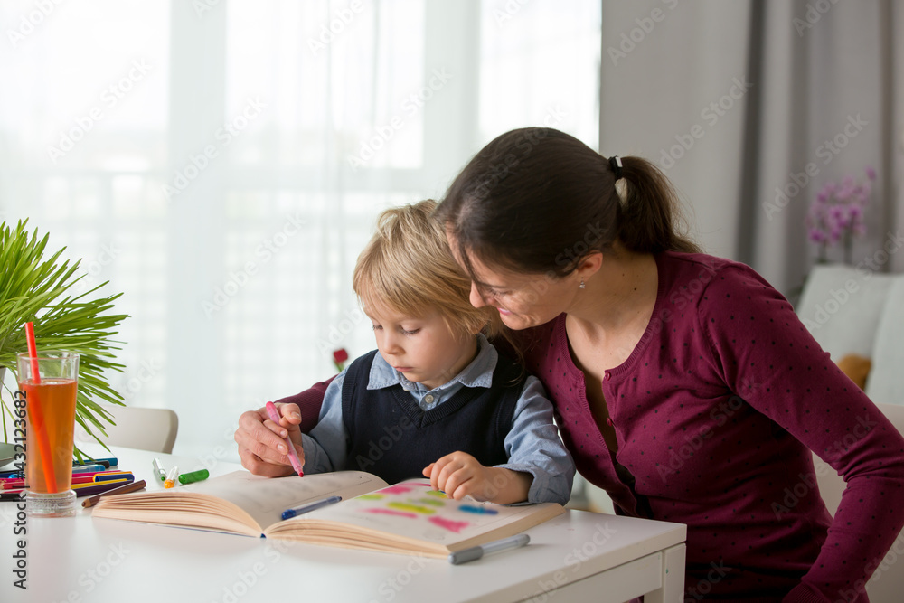 Cute preschool child, blond boy, filling some homework in a work book and coloring, mother helping him Cute preschool child, blond boy, filling some homework in a work book and coloring, mother helping him