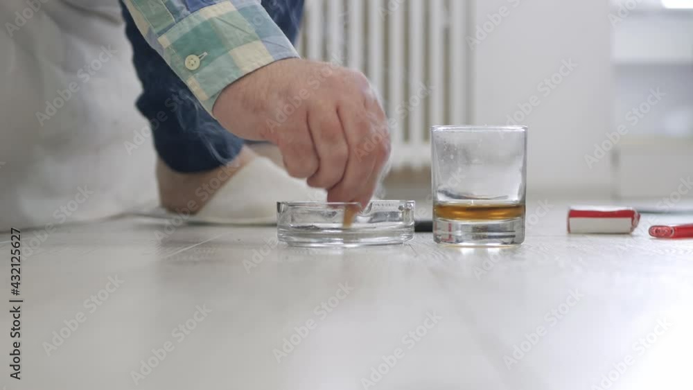Adult Person Wearing Slippers, Sitting on the Bed, Finish His Cigarette and the Glass with Alcohol. Adult Person Wearing Slippers, Sitting on the Bed, Finish His Cigarette and the Glass with Alcohol.