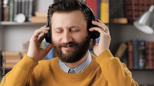 Man with headphones listens to music. Positive bearded man in black wireless headphones holds his head with his hands and enjoys music