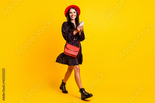 Full length photo of sweet charming lady dressed black clothes cap walking typing gadget isolated yellow color background