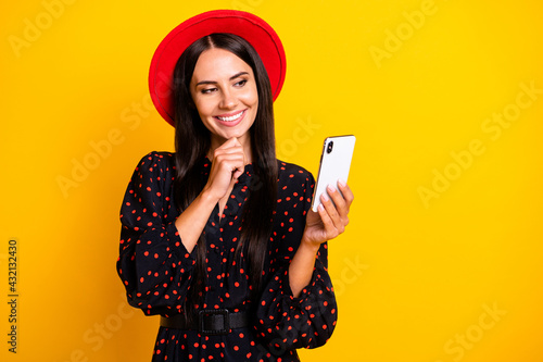 Photo of pretty thoughtful young lady dressed black clothes cap chatting modern gadget arm chin isolated yellow color background