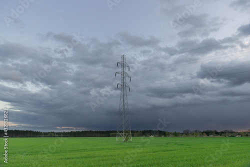 Elektryczny słup wysokiego napięcia na tle pokrytego ciemnymi, groźnymi chmurami nieba.