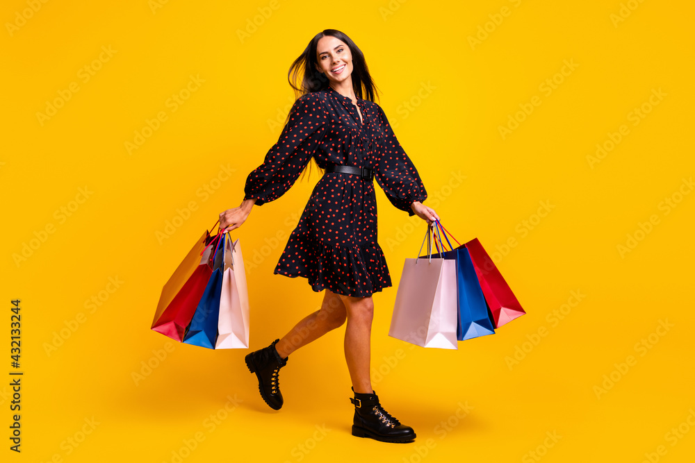 Full length body size view of attractive cheerful girl holding in hands new things walking isolated over bright yellow color background