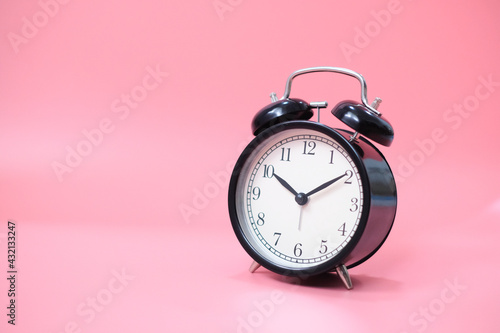 Black vinatge alarm clock with pink background.