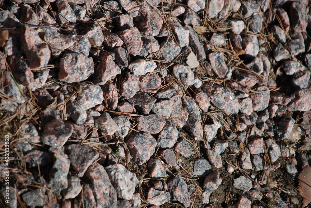 Small granite stones lie on the ground. A scattering of small granite stones of various shapes lying on a flat surface. Multi-colored stones consist of shades of brown, red, gray, black. Small granite stones lie on the ground. A scattering of small granite stones of various shapes lying on a flat surface. Multi-colored stones consist of shades of brown, red, gray, black.