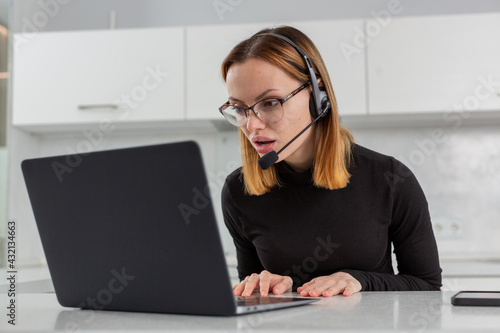 a girl in a black jacket and glasses stares at the computer screen in surprise, sitting at the kitchen table. Remote work. Home schooling. High quality photo
