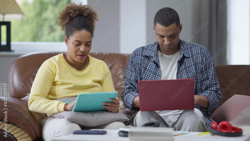 Surprised African American man rolling eyes as flirting woman talking holding payment card. Portrait of busy confident handsome husband working online in home office distracted by wife Surprised African American man rolling eyes as flirting woman talking holding payment card. Portrait of busy confident handsome husband working online in home office distracted by wife
