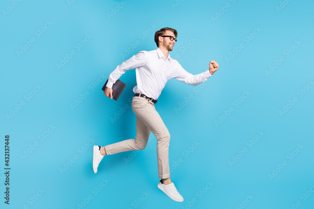 Full length body size view of attractive cheerful man jumping running carrying laptop isolated over bright blue color background Full length body size view of attractive cheerful man jumping running carrying laptop isolated over bright blue color background