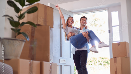 Bilde på lerret Man Carrying Woman Over Threshold Of New Home As Couple Move In Together