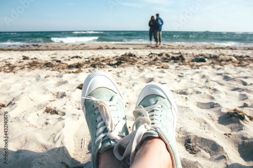 Girl in green sneakers resting on the beach. Summer beach and sea. Stormy sea, ocean