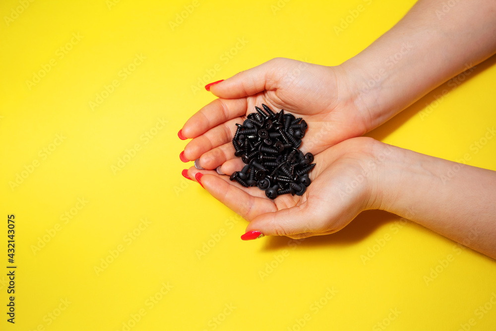 Screws in the hands of a girl on a yellow background in a close-up view from above, a slide of iron, Screws in the hands of a girl on a yellow background in a close-up view from above, a slide of iron,