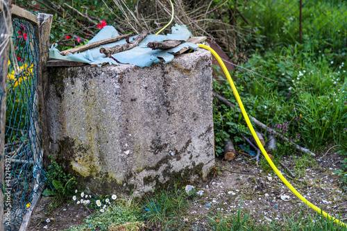 Old water well with a plastic hose for irrigation in a garden on a sunny spring day in the countryside