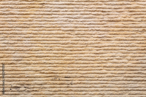 Yellow textured sand background, stone wall with horizontal wavy lines, in close-up