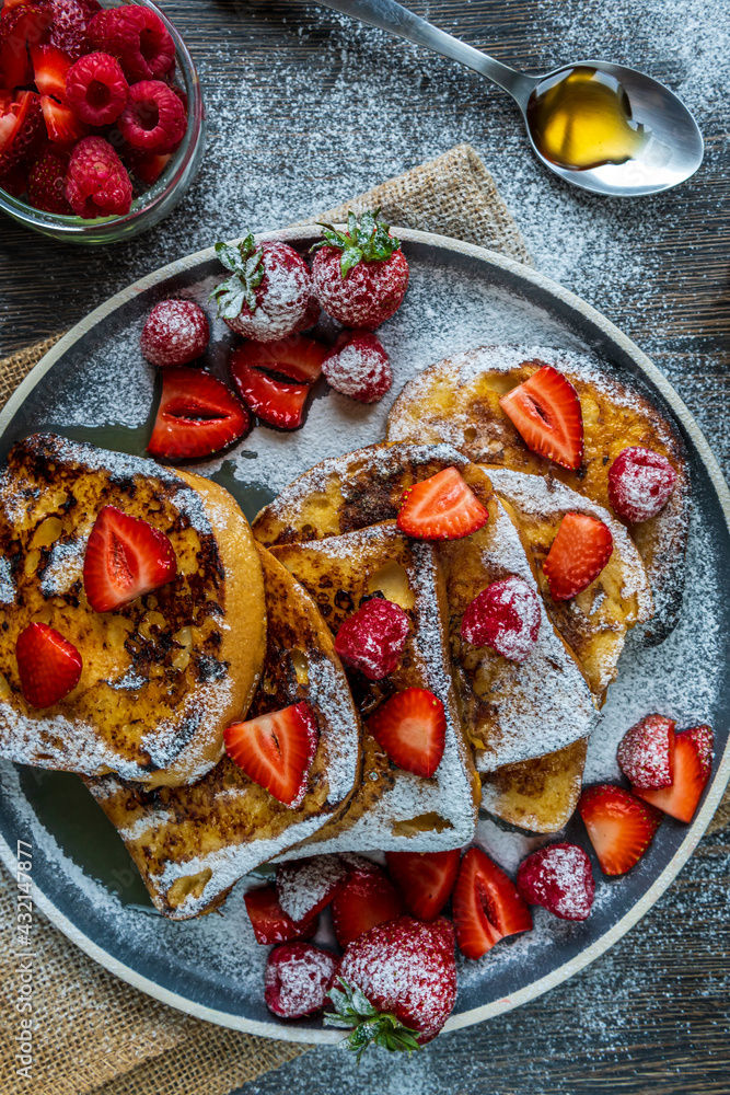 French toast with fresh strawberries, raspberries, maple syrup, and powdered sugar on a plate. Tasty morning breakfast or brunch with gluten free bread. Easy making and healthy dessert. Top view