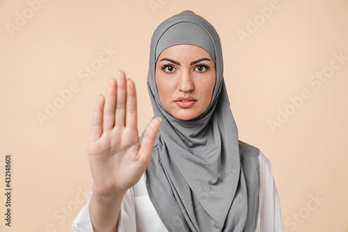 Nice-looking young serious islamic arabian middle eastern muslim woman in grey hijab showing stop warning sign isolated over beige background. Forbidden, prohibited concept, saying no photo