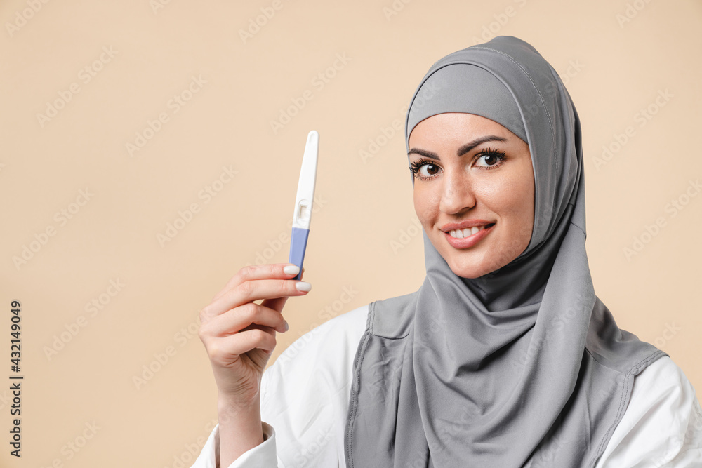 Happy young arabian muslim islamic woman wearing grey hijab holding pregnancy test isolated over white background. Positive pregnancy test, expecting a baby, future mom, fertility natality concept - obrazy, fototapety, plakaty 