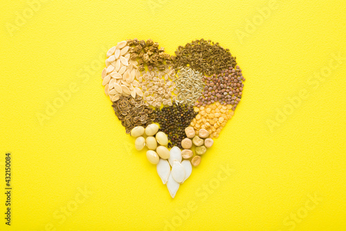 Heart shape created from dry different seeds on bright yellow table background. Closeup. Top down view.