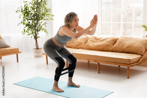 Fit sporty african-american woman doing fitness exercises at home. Slim young African American girl takes care about her health, does sports at home on fitness mat, does sit-ups with rubber band © InsideCreativeHouse