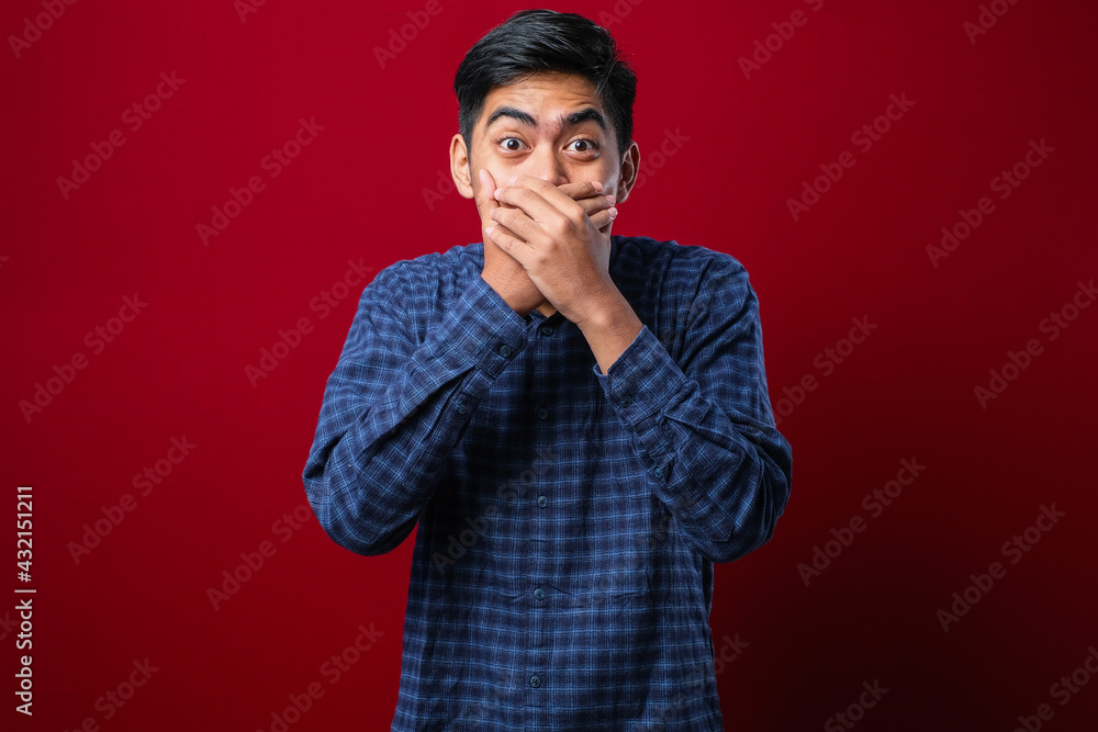 Young handsome man wearing flanel shirt over isolated red background shocked covering mouth with hands for mistake Young handsome man wearing flanel shirt over isolated red background shocked covering mouth with hands for mistake