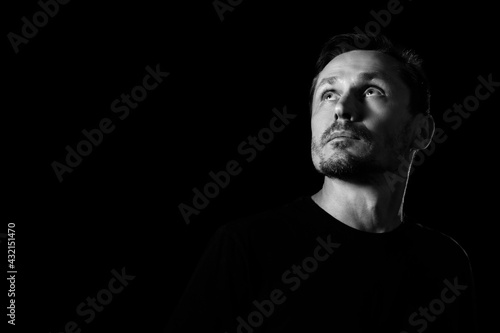 Black and white portrait of an unshaven sad man in a pensive mood looking up. Isolated on black. Copyspace.