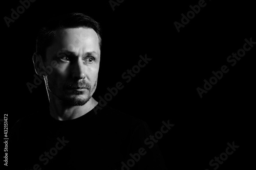 Black and white portrait of an unshaven sad man in a pensive mood looking away. Isolated on black. Copyspace.