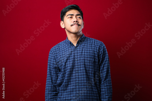 Young handsome man wearing casual shirt over isolated red background looking away to side with smile on face, natural expression © Reza